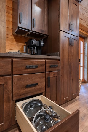 A kitchen with wooden cabinets, a coffee maker, and a drawer with pots.