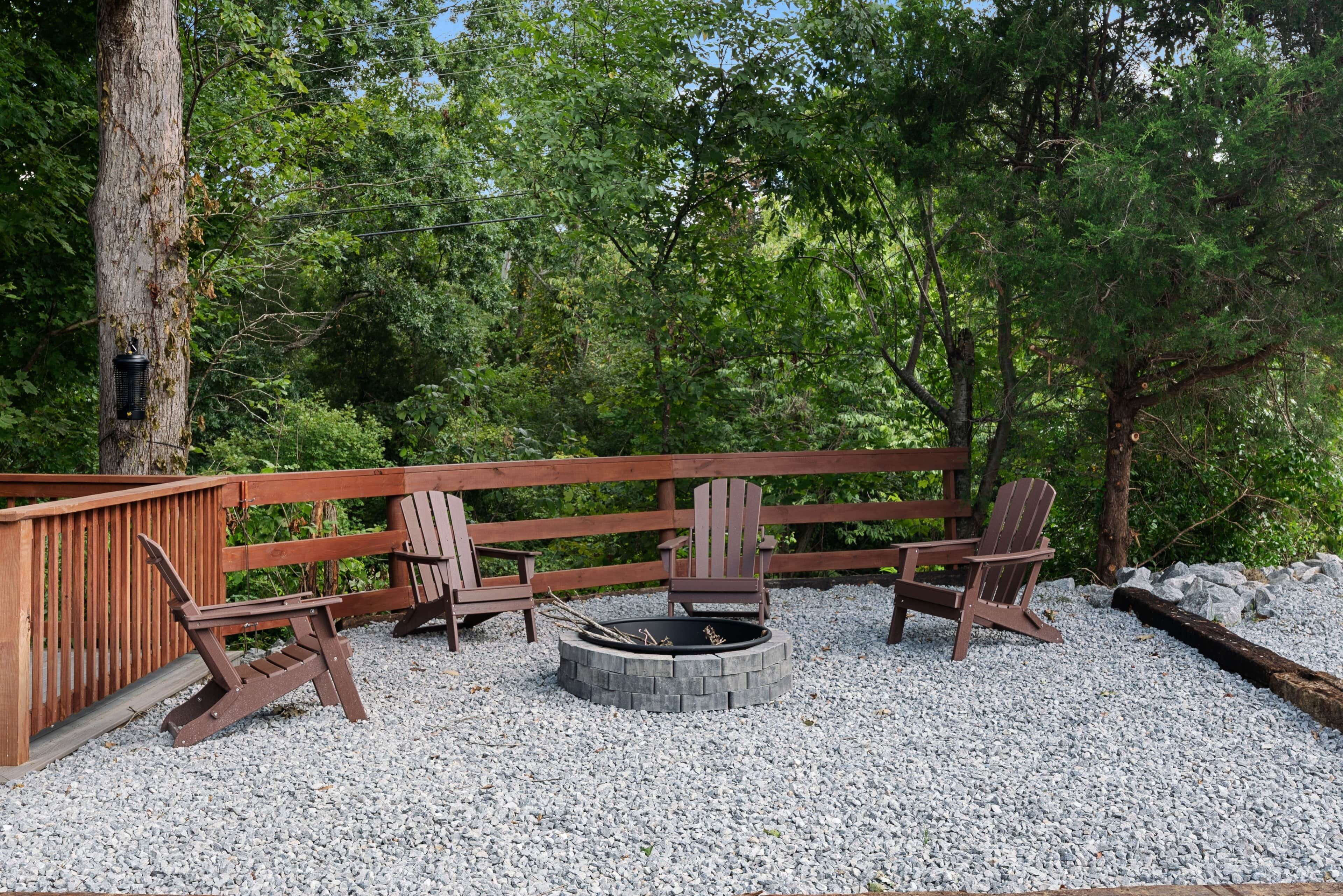 Una terraza de madera con sillas Adirondack y un hogar para fogata rodeado de grava.