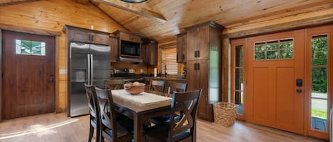 A wooden interior with a kitchen, dining table, chairs, and a refrigerator.