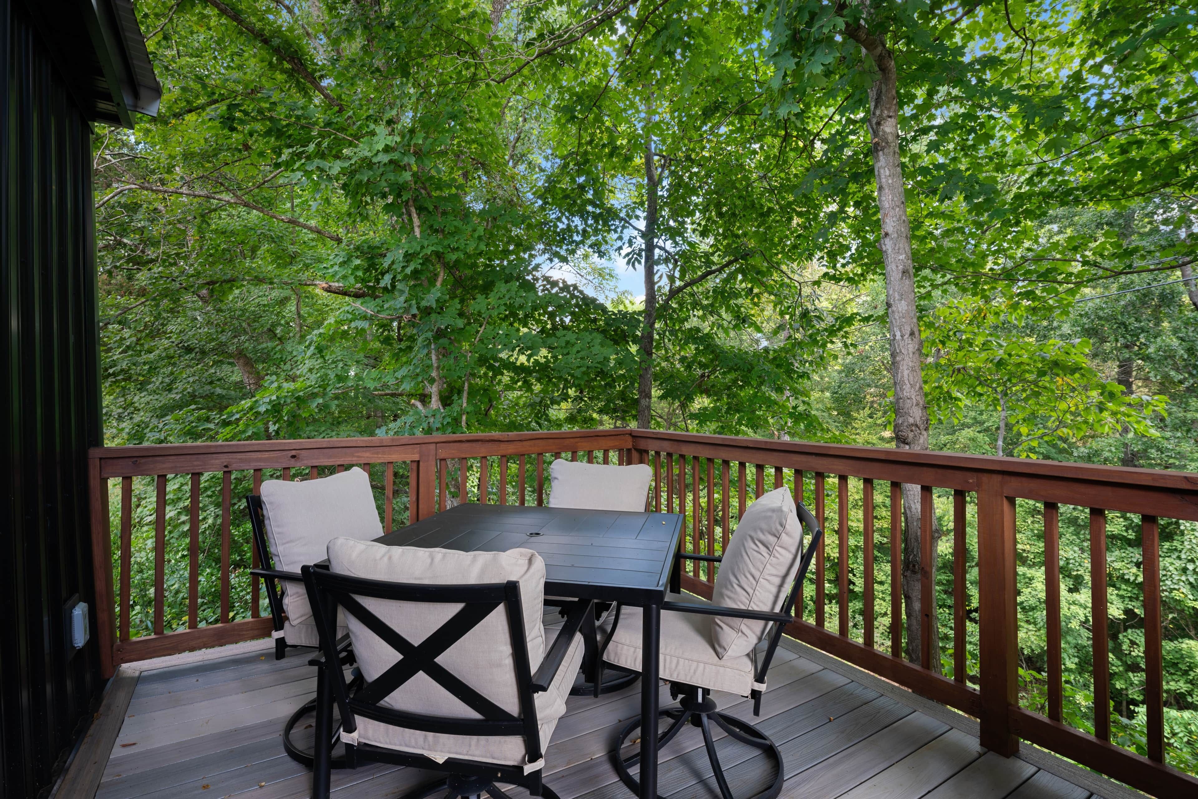 A wooden deck with a table and chairs, surrounded by trees.
