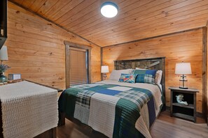 Ein Zimmer mit Holzwänden, einem Bett, zwei Nachttischen mit Lampen, einem Beistelltisch und einem kleinen Regal mit Dekoration.
