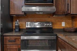Cozinha com forno de aço inoxidável, armários de madeira e micro-ondas.