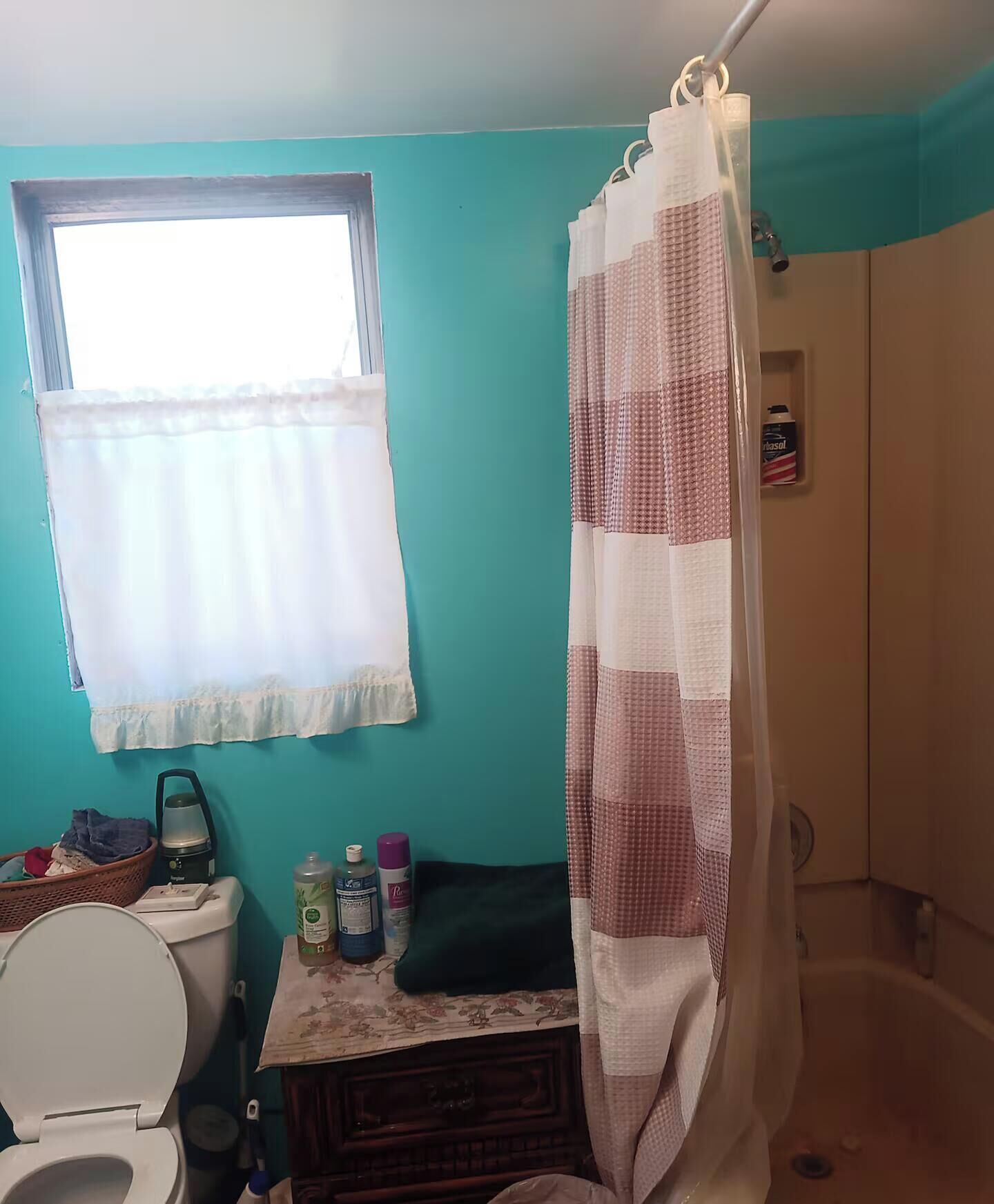 A bathroom with a toilet, a sink, a window with a curtain, and a shower curtain.