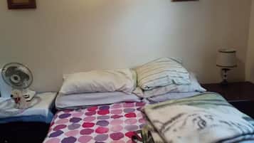 Una camera da letto con un letto, due cuscini, una ventola sul comodino e una lampada.