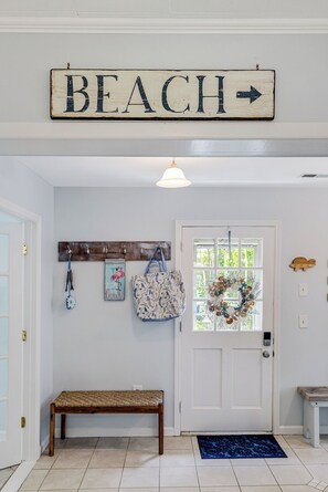A hallway with a 'BEACH' sign, a bench, a coat rack with items, and a door with a wreath. - Seahorse Stables - Spotless Coastal Cottage - 0.5 mile to Beach -  Sleeps 8 (Oak Island)
