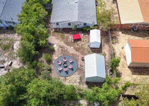 An aerial view of a residential area with houses, a circular outdoor seating area with chairs, and a small shed. - Seahorse Stables - Spotless Coastal Cottage - 0.5 mile to Beach -  Sleeps 8 (Oak Island)