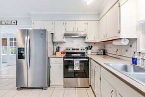 A modern kitchen with stainless steel appliances, white cabinetry, and a tiled backsplash. - Seahorse Stables - Spotless Coastal Cottage - 0.5 mile to Beach -  Sleeps 8 (Oak Island)