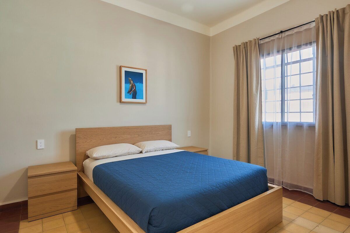 Una camera da letto con un letto in legno, un comodino, un quadro appeso alla parete e una finestra con tende.