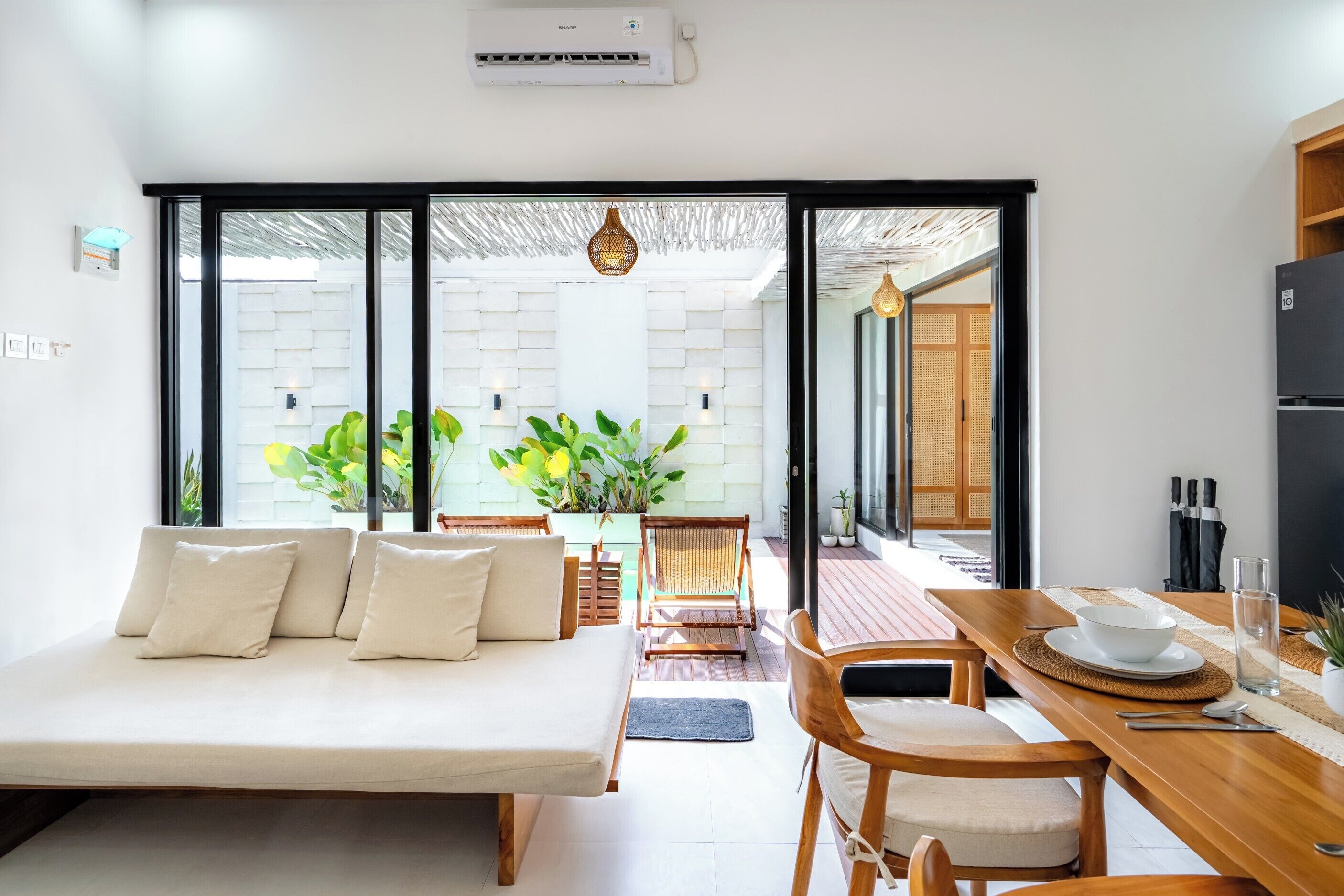 A modern room with a sofa, dining table, chairs, and a view through large glass doors.
