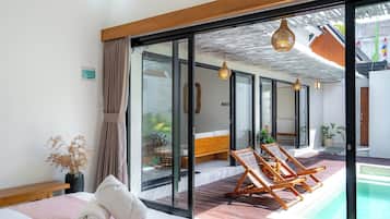 Una habitación moderna con una cama, un ventanal que da a una zona de piscina y dos sillones de descanso.