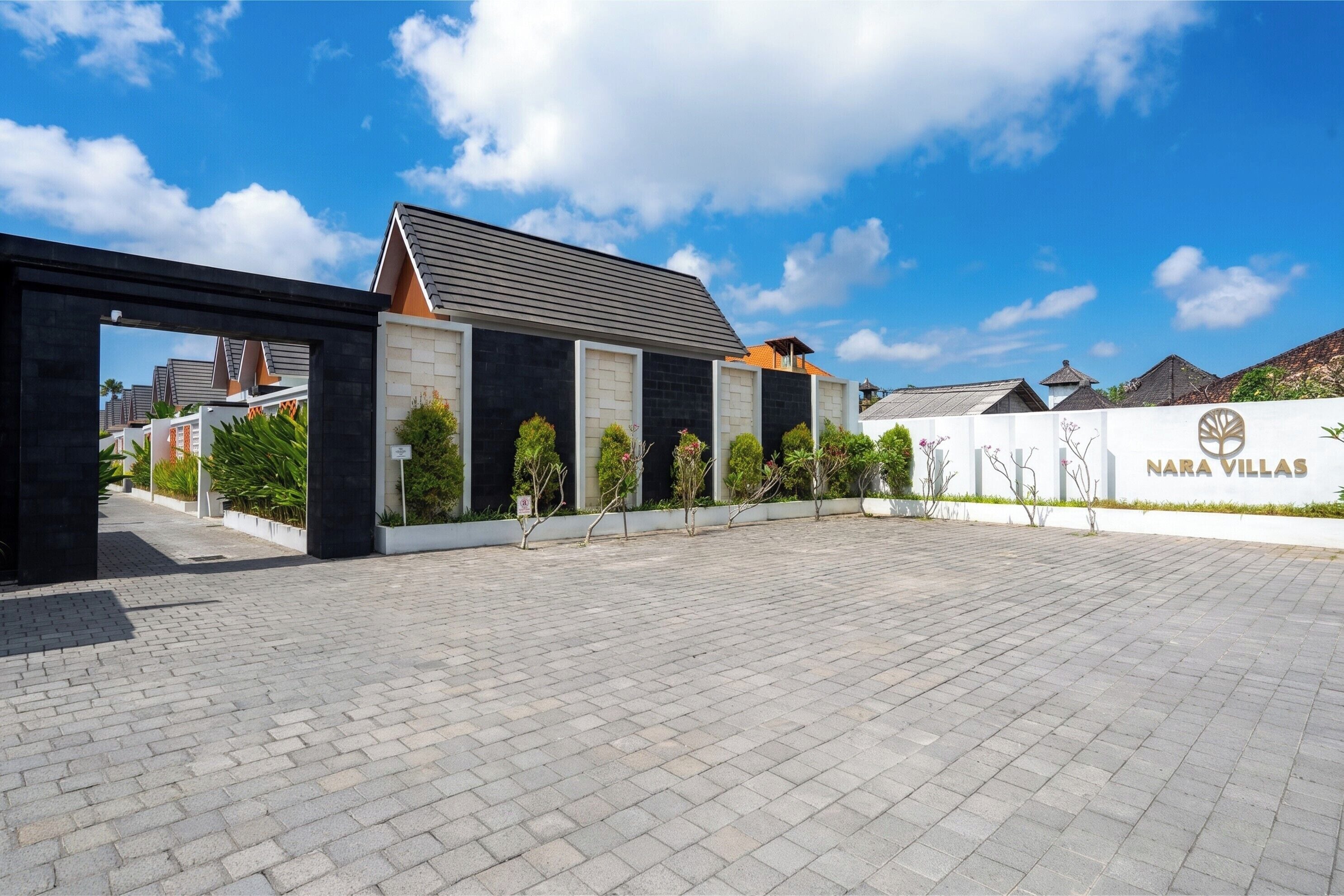 A paved entrance area with a modern building featuring a dark facade and a sloped roof.