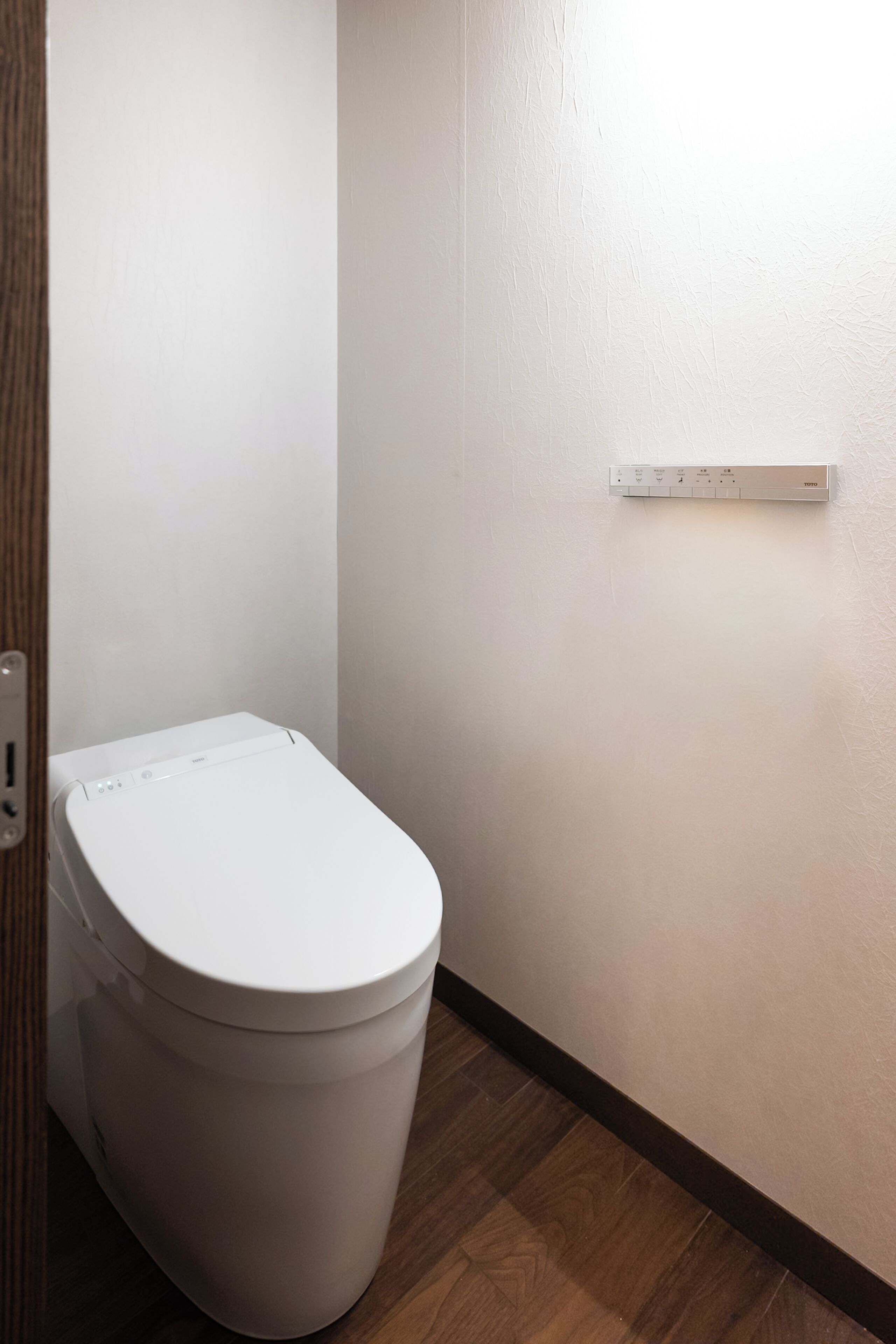 A white toilet in a bathroom with a wooden floor and a white wall.