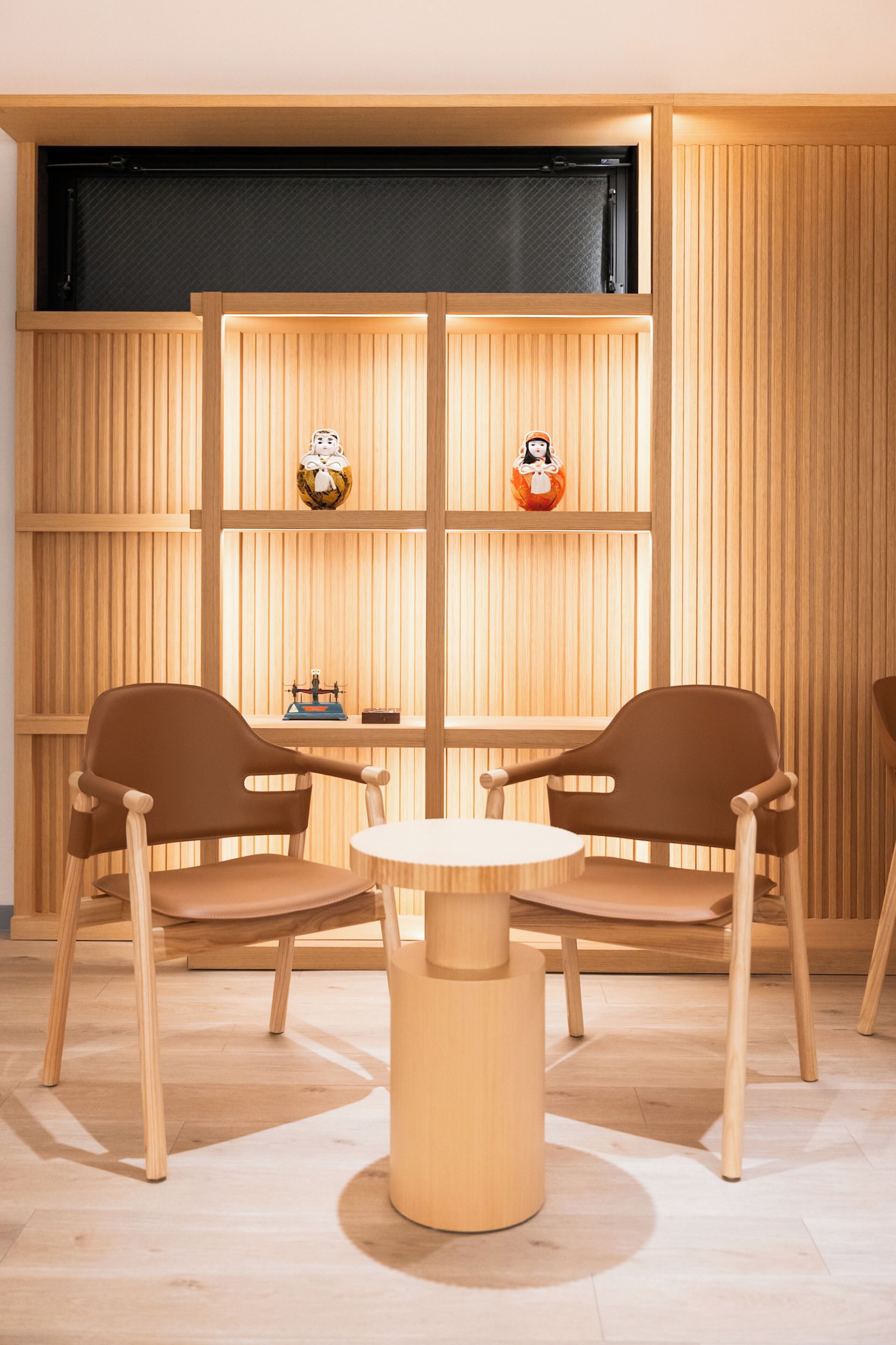A room with two brown chairs around a round table, wooden panel walls, and two small figurines on shelves.
