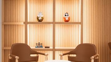 A room with two brown chairs around a round table, wooden panel walls, and two small figurines on shelves.