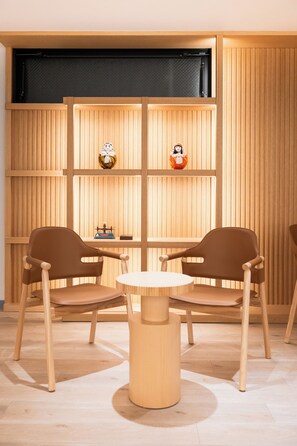 Una habitación con dos sillas marrones alrededor de una mesa redonda, paredes de paneles de madera y dos pequeñas figuras en estantes.