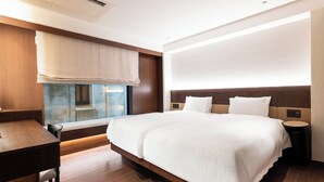 Una habitación de hotel moderna con una cama grande, mesitas de noche, un escritorio y una ventana con vistas.