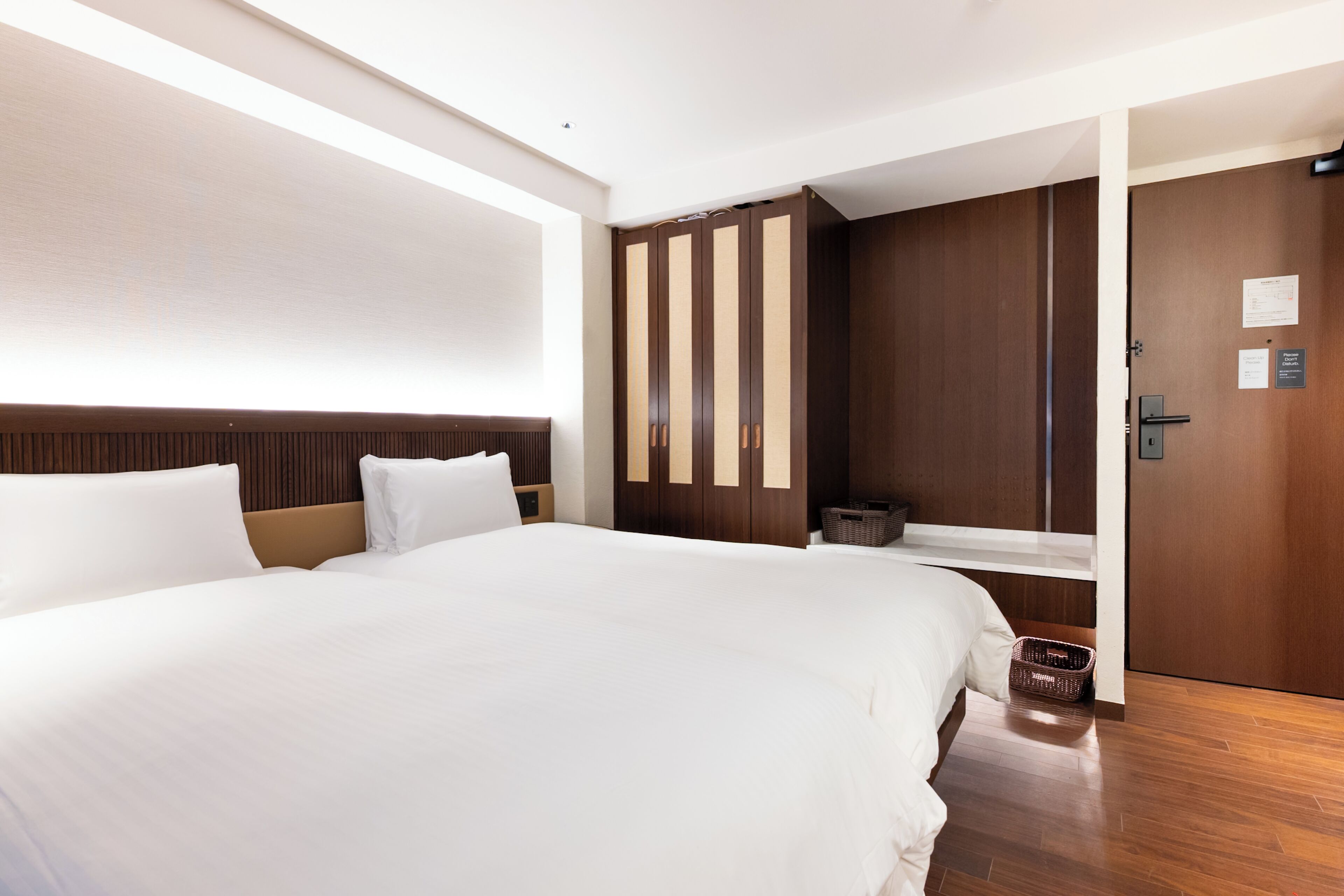 A hotel room with a large bed, a wooden wardrobe, and a door with a sign.