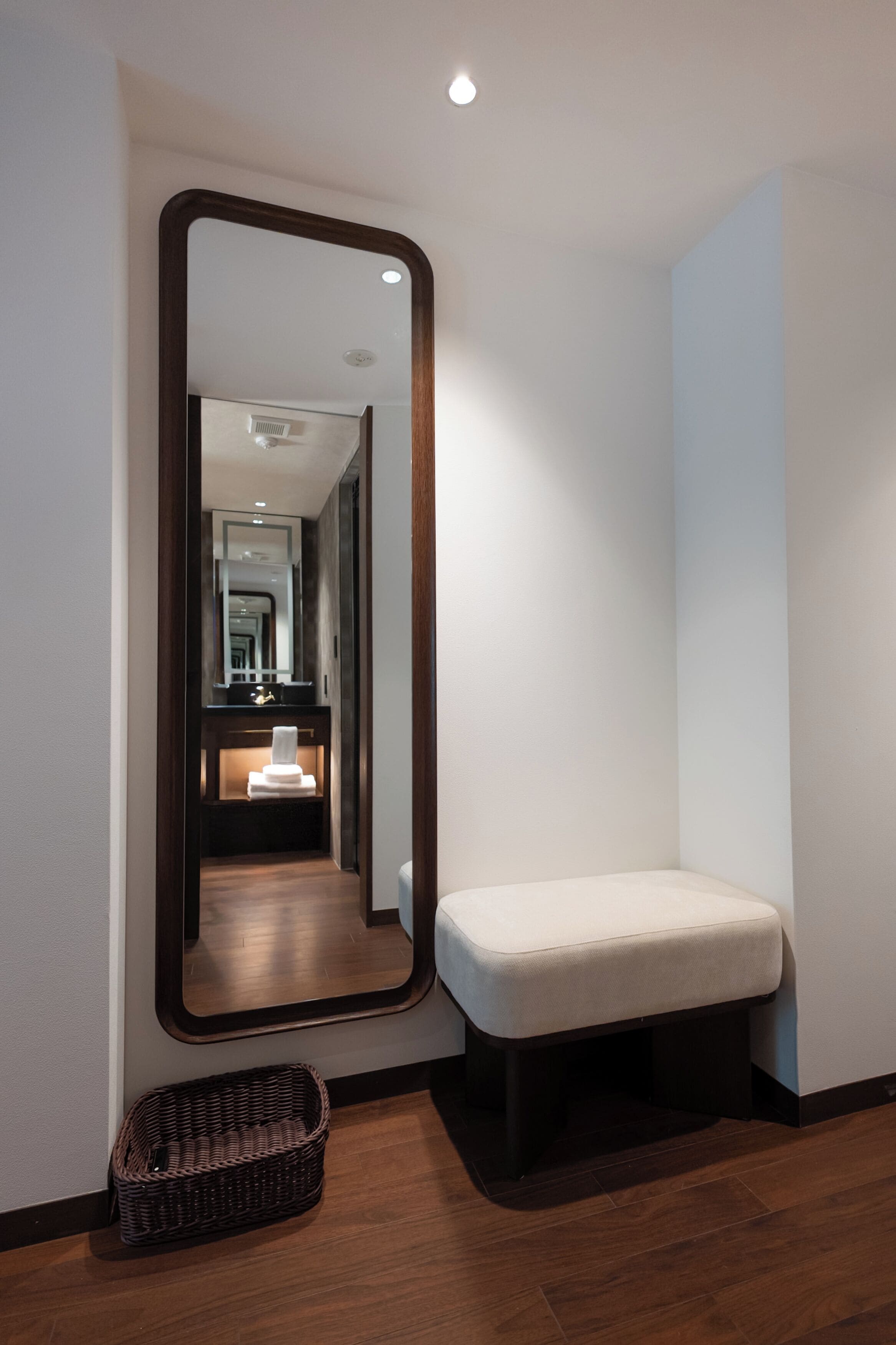Un couloir avec un grand miroir, un banc et un panier en osier.