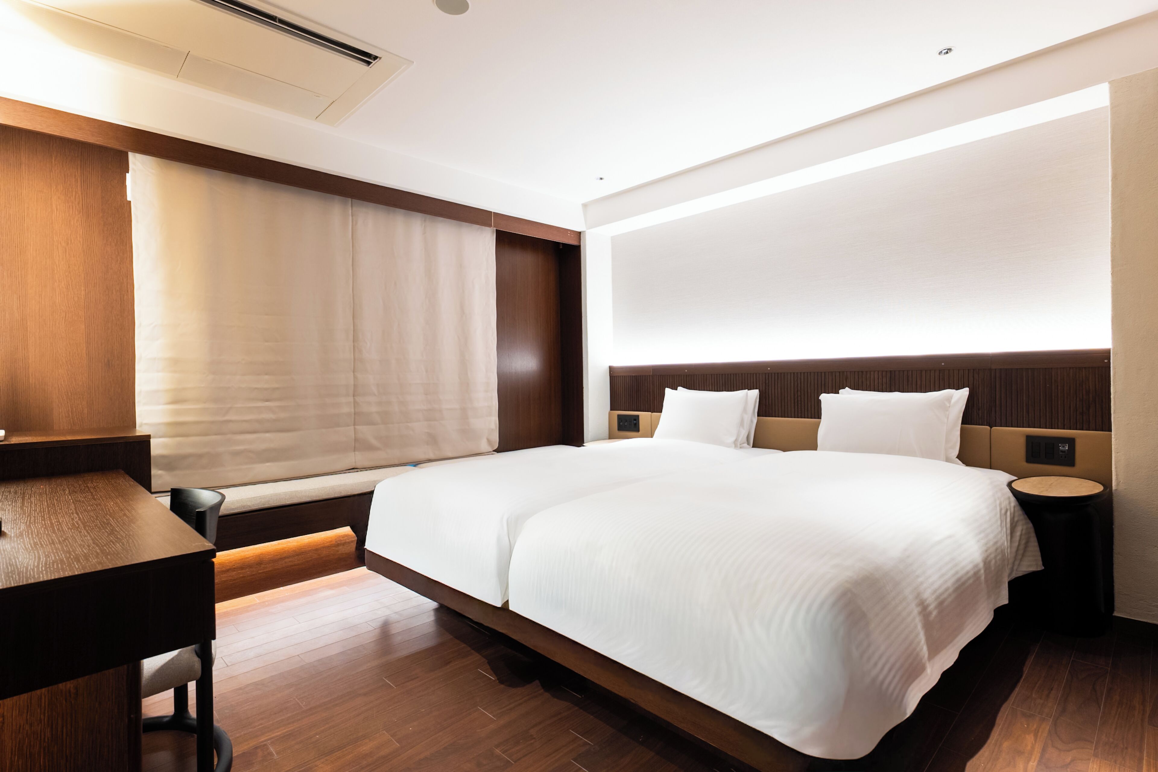 Una habitación de hotel moderna con una cama grande, mesitas de noche, un escritorio y una ventana con cortinas.