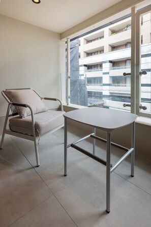 Een kamer met een enkele stoel en een tafel, een groot raam met uitzicht op een gebouw en een eenvoudige muur.