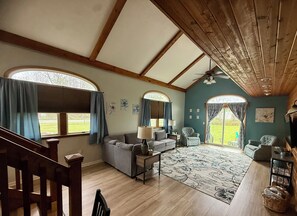 Amplia sala de estar con techo alto, vigas de madera, un ventanal y vistas al exterior.