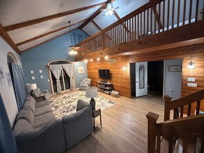 A spacious living room with a high ceiling, wooden beams, a sofa, a television, and a staircase. -     Balti Bay Loft -Beach & Boating Getaway Downtown New Baltimore  -Sleeps 11 (New Baltimore)