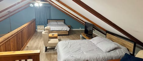 Une chambre avec un plafond en pente, un lit, un bureau, une chaise et un ventilateur de plafond.