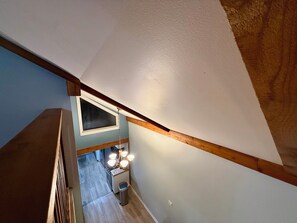 Una escalera con vigas de madera y vistas a una zona de cocina con ventana y lámpara.