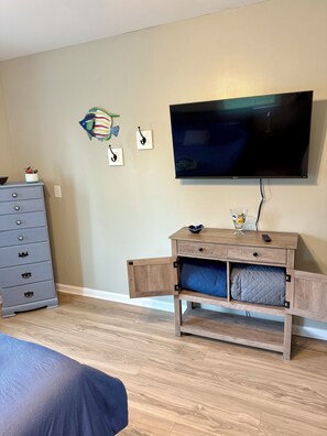 A room with a television mounted on the wall, a wooden cabinet with drawers, a dresser, and a bed with a blue bedspread. -     Balti Bay Loft -Beach & Boating Getaway Downtown New Baltimore  -Sleeps 11 (New Baltimore)