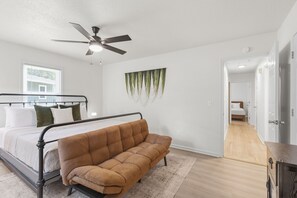 A bedroom with a bed, a sofa, a ceiling fan, a window, and a door leading to another room. - 3/2 Retreat, Walk to DT Simpsonville, Fire Pit (Simpsonville)