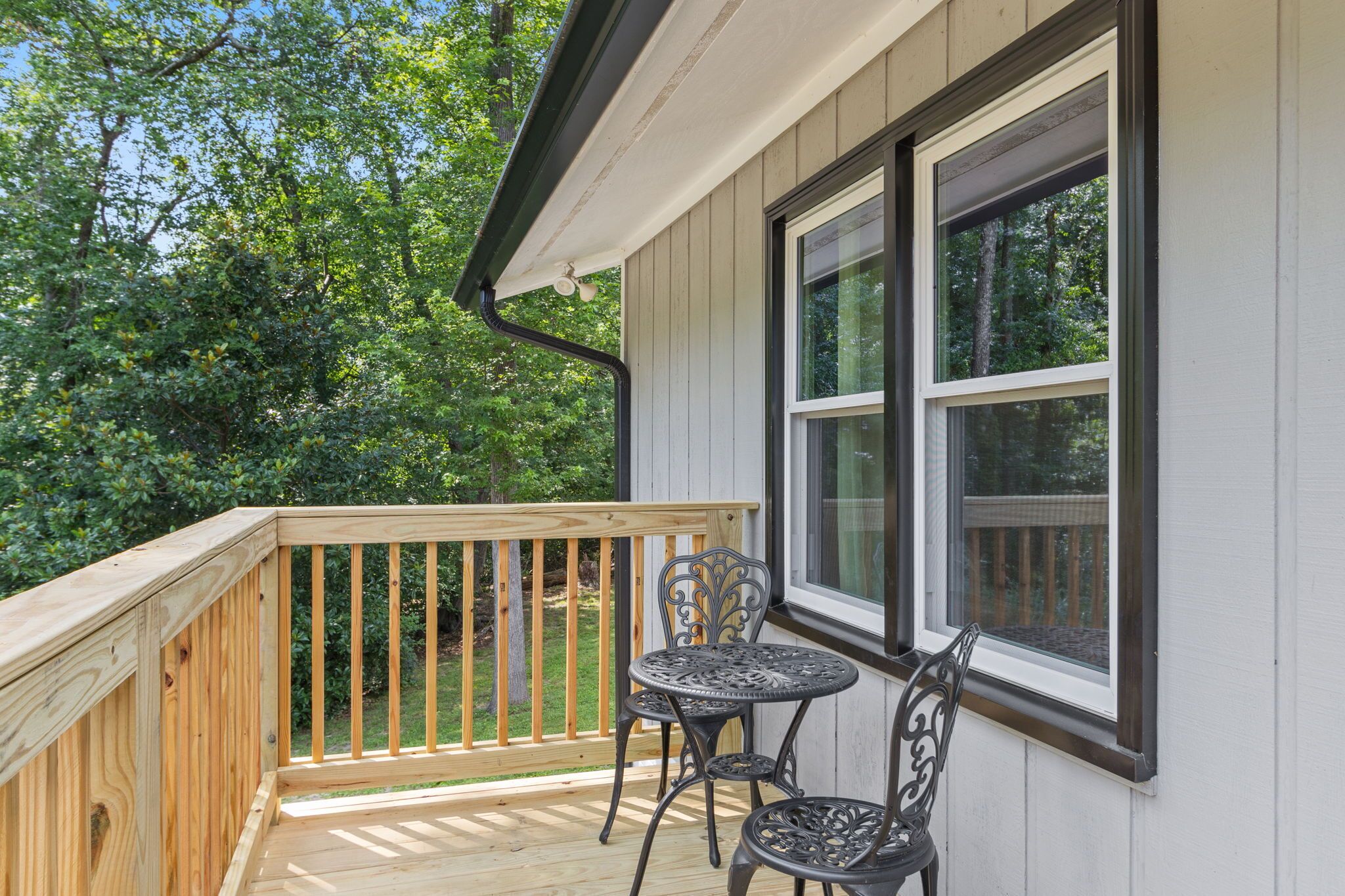 A wooden deck with a railing, two metal tables, and chairs.