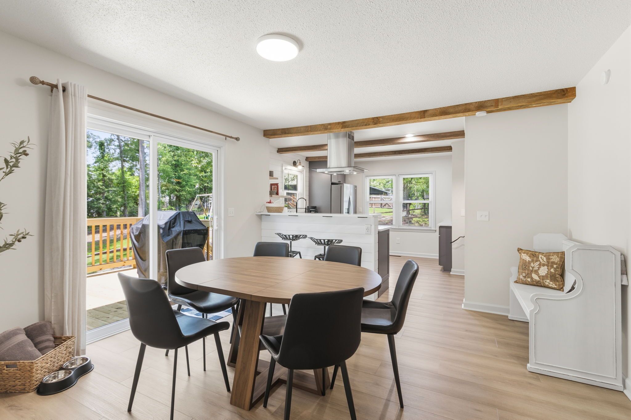 Una cocina moderna con una isla central, un comedor con una mesa redonda y sillas, y vistas al exterior a través de amplios ventanales correderas.