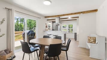 Una cocina moderna con una isla central, un comedor con una mesa redonda y sillas, y vistas al exterior a través de amplios ventanales correderas.