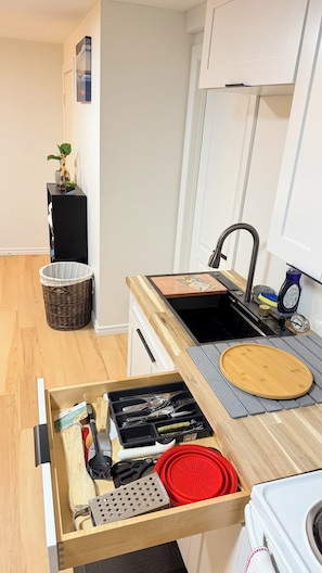 Eine Küche mit einer Holzausziehtafel, einem Spülbecken, einer Schublade mit Besteck und einem Korbwannenkorb.