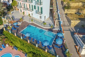 Et tagområde med swimmingpool, flere liggestole og parasoller, samt en bygning med altaner.