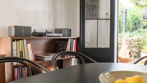 Ein Zimmer mit einem Holztisch, Stühlen, einem Bücherregal und einer Tür, die in einen Garten führt.