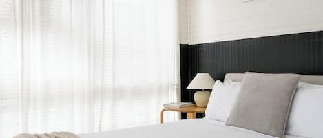 A hotel room with a bed, a nightstand, a lamp, and sheer curtains.