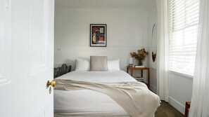 A bedroom with a bed, a bedside table with a lamp, a mirror, and a framed picture on the wall. - Sisteron | Daylesford (Daylesford)
