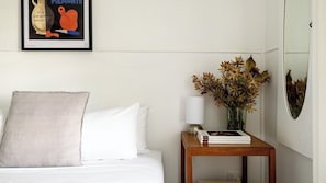 Une chambre d’hôtel avec un lit, une table de chevet avec une lampe, un vase contenant des fleurs séchées et un tableau encadré au mur.