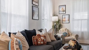 Ein Wohnzimmer mit einer Couch, einer Lampe und gerahmten Reiseplakaten an der Wand.