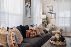 Ein Wohnzimmer mit einer Couch, einer Lampe und gerahmten Reiseplakaten an der Wand.