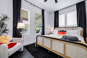 Ein modernes Schlafzimmer mit einem Bett, einem Sessel, einer Lampe und einem Fenster mit Jalousien.