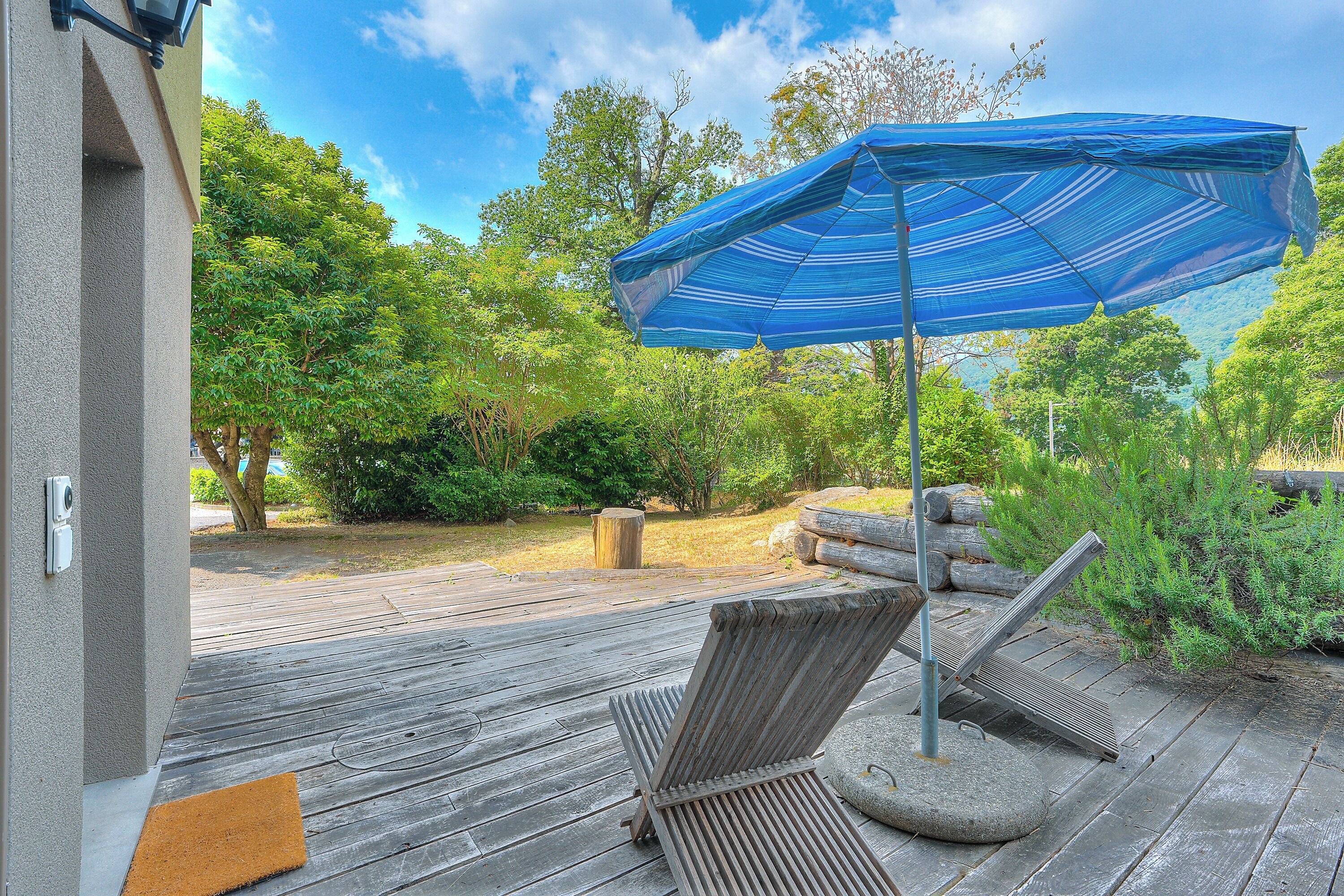 Een houten terras met twee ligstoelen en een blauwe parasol.