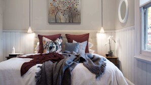 Um quarto com cama, travesseiros, cobertor, pintura, janela e mesa de cabeceira.