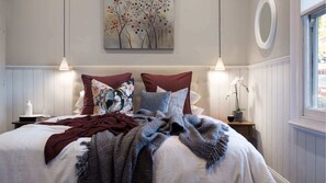 A bedroom with a bed, pillows, a blanket, a painting, a window, and a nightstand. - Albert Cottage Daylesford (Daylesford)