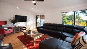 Ein modernes Wohnzimmer mit einem schwarzen Ledersofa, einem roten Sessel, einem Couchtisch und einem an der Wand befestigten Flachbildfernseher.