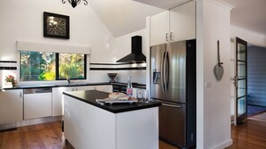 Une cuisine moderne dotée d’un îlot central, d’appareils électroménagers en acier inoxydable et d’une grande fenêtre offrant une vue sur la verdure.