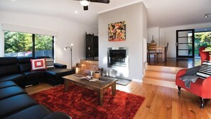 Un salon moderne avec une cheminée, un canapé en cuir noir, un fauteuil rouge et un tapis rouge.