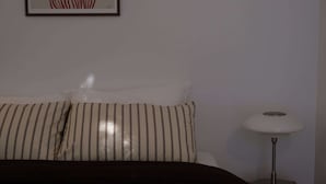 Ein Bett mit gestreifter Bettwäsche, einem weißen Kopfkissen und einer Nachttischlampe.