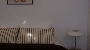 Ein Bett mit gestreifter Bettwäsche, einem weißen Kopfkissen und einer Nachttischlampe.